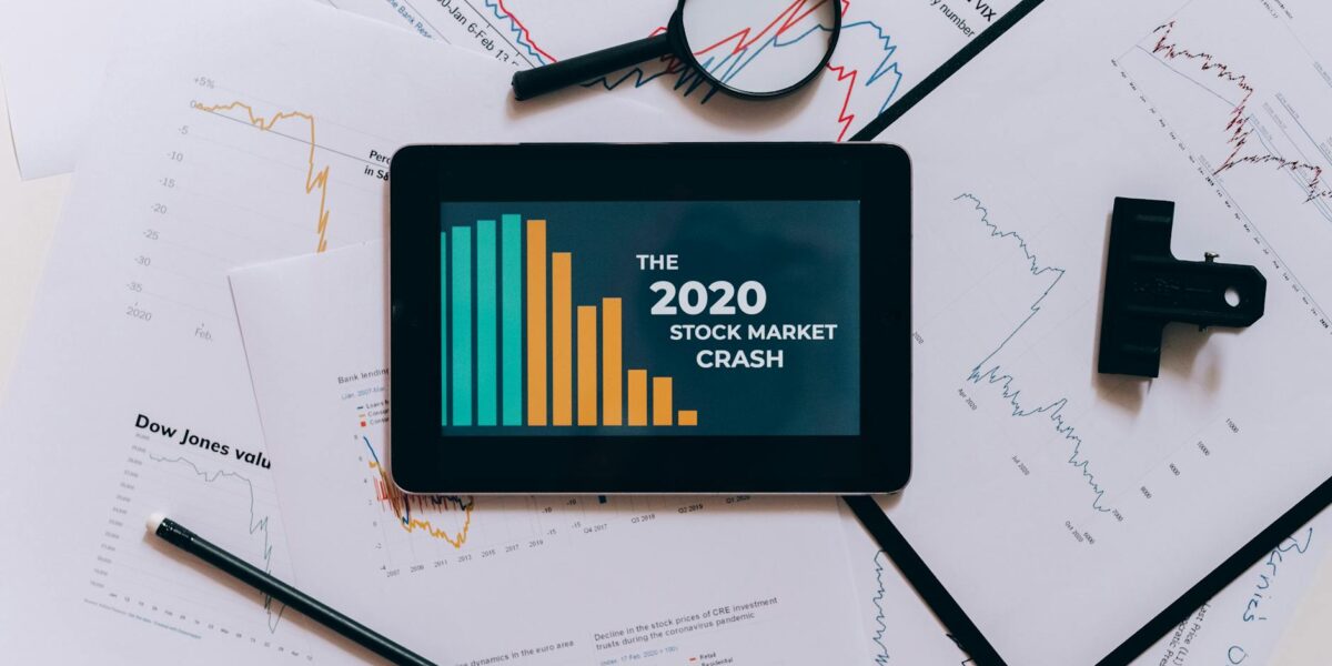 Flat lay of tablet showing 2020 stock market crash with charts and papers.