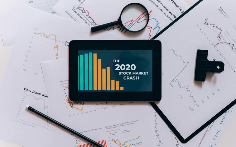 Flat lay of tablet showing 2020 stock market crash with charts and papers.