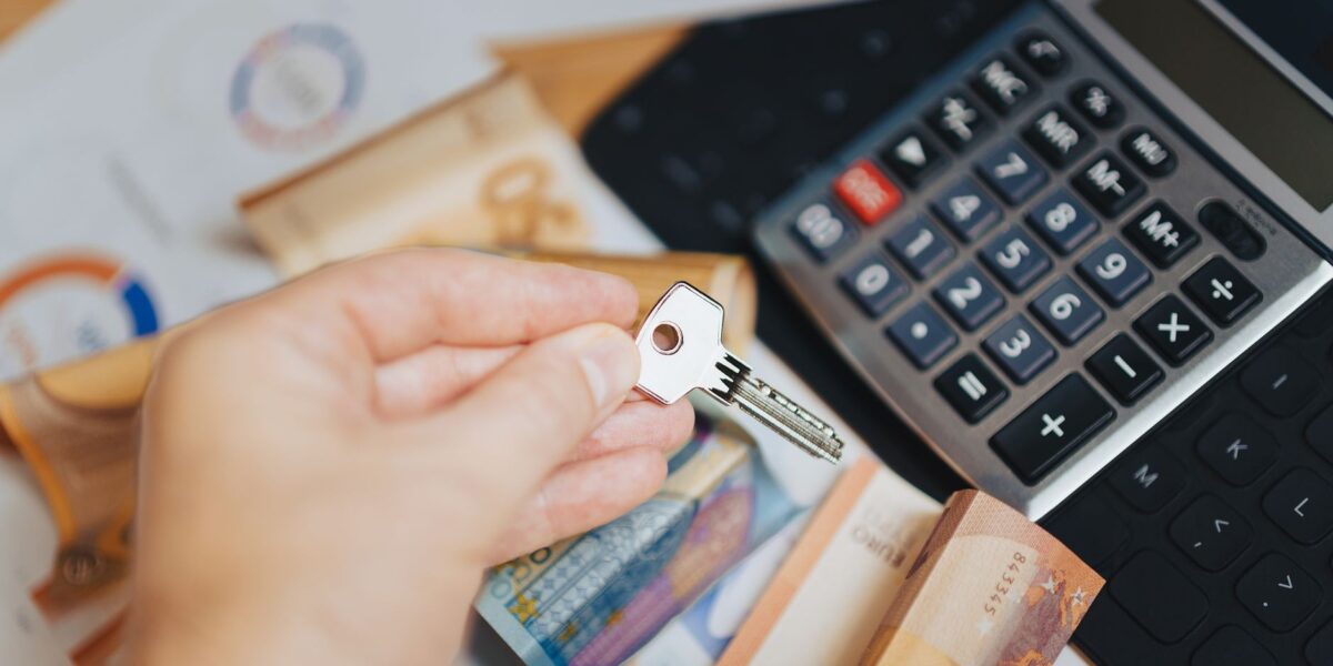 Hand holding key above Euro banknotes and calculator, symbolizing real estate investment.