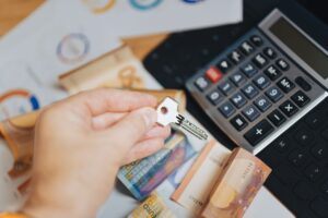 Hand holding key above Euro banknotes and calculator, symbolizing real estate investment.