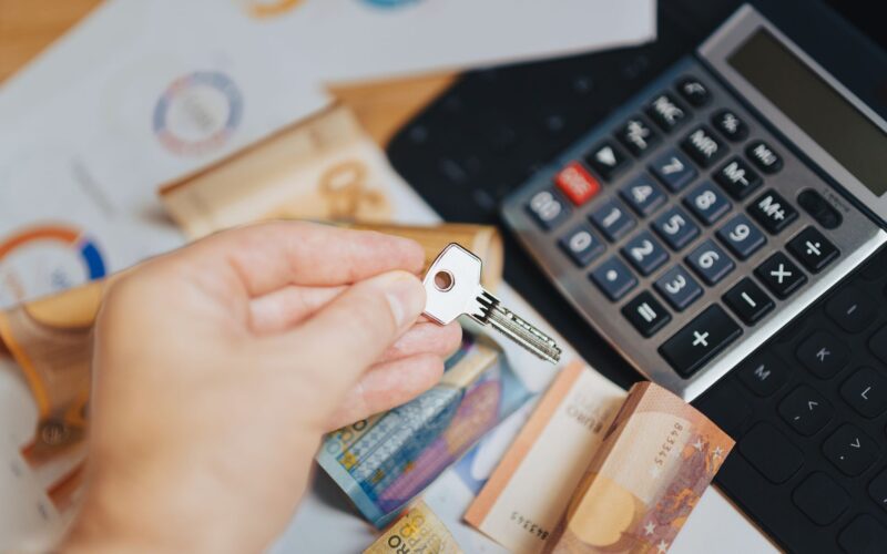 Hand holding key above Euro banknotes and calculator, symbolizing real estate investment.