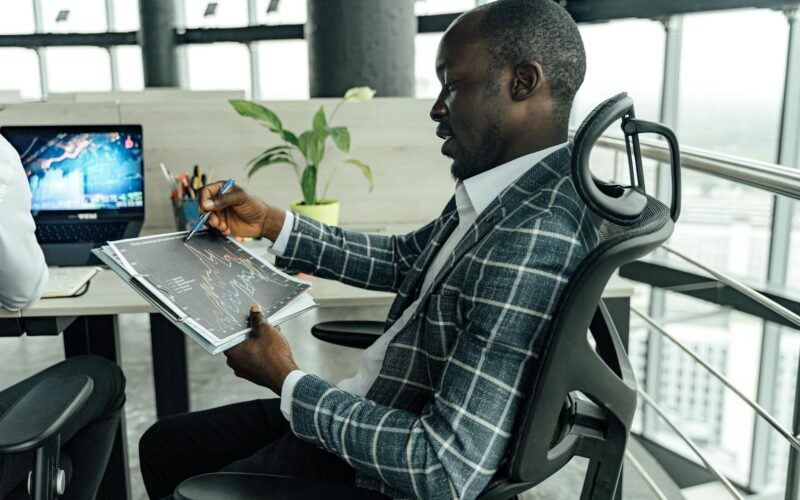 A businessman in a stylish suit reviews financial charts in a modern office setting.