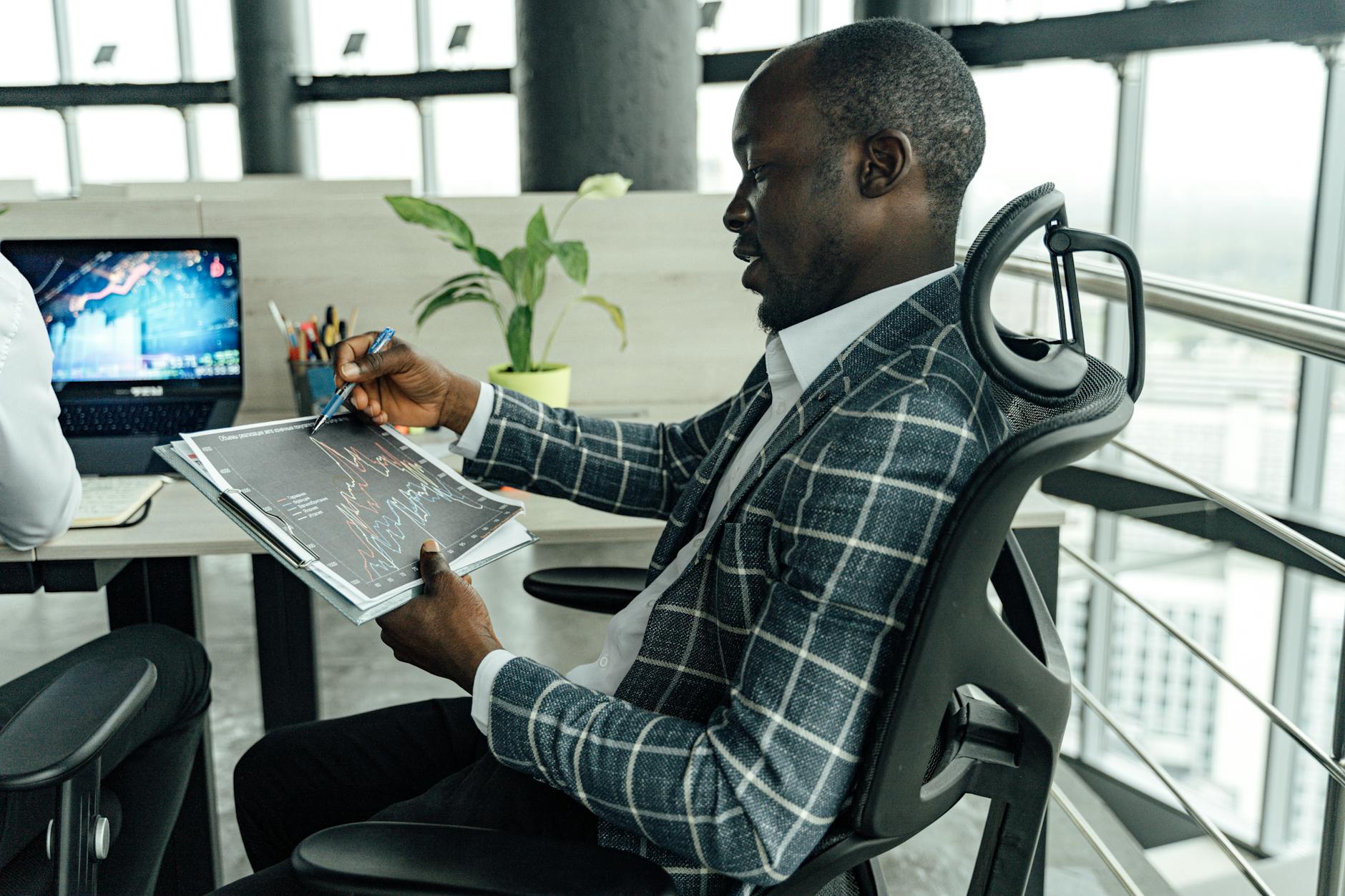 A businessman in a stylish suit reviews financial charts in a modern office setting.