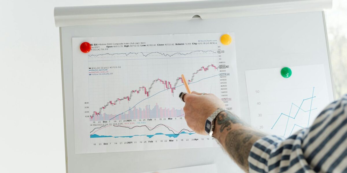 A tattooed person pointing at finance charts and graphs on a whiteboard.