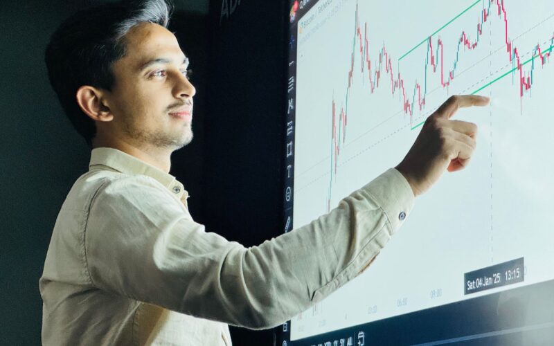 Man analyzing stock market graph on a digital board with a focused expression.