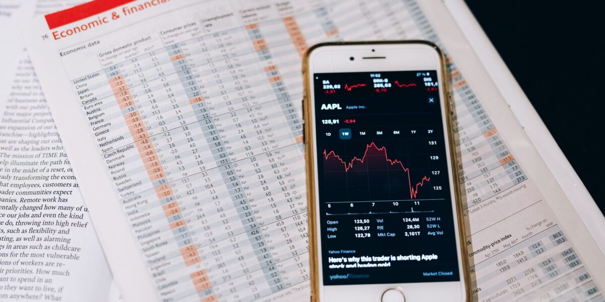 Smartphone displaying stock market data on papers with financial charts.