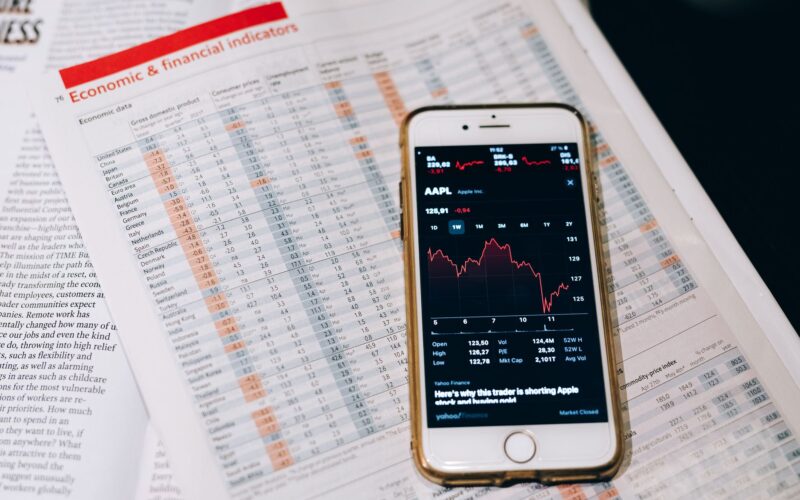 Smartphone displaying stock market data on papers with financial charts.