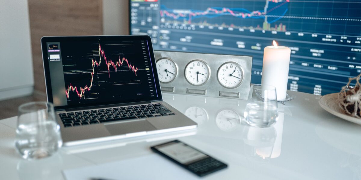 A modern workspace featuring financial charts and multiple clocks on a white table, ideal for trading.