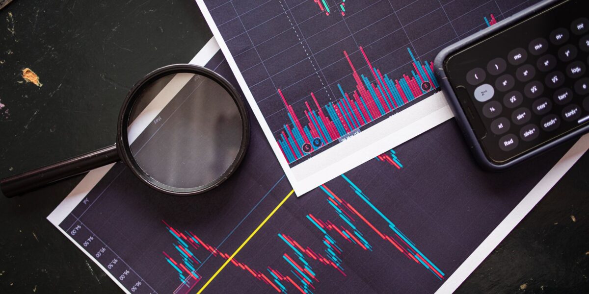 Stock market charts analyzed with a magnifying glass and calculator for financial research.