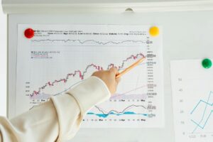 Close-up of a woman's hand pointing to data trends on a stock market chart using a pencil.