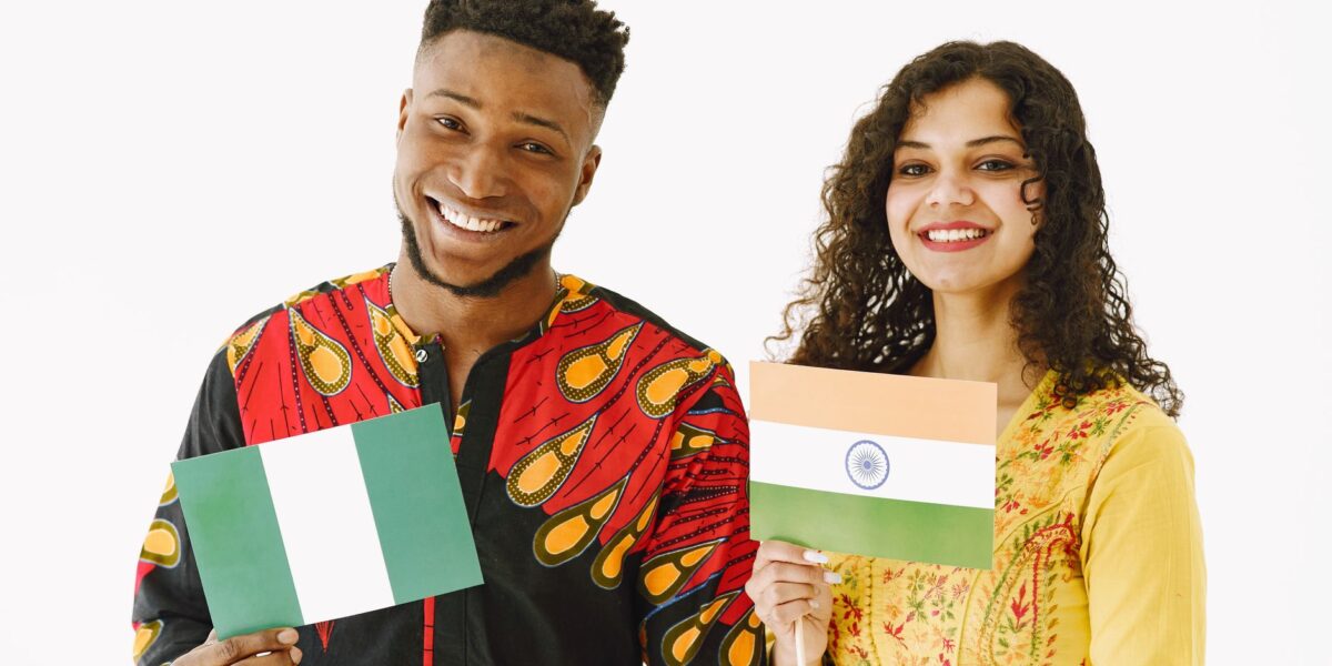 A Nigerian man and Indian woman smiling while holding their country's flags indoors.