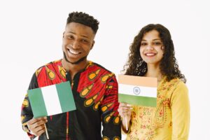 A Nigerian man and Indian woman smiling while holding their country's flags indoors.