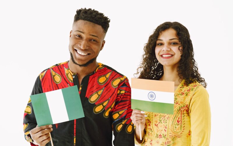 A Nigerian man and Indian woman smiling while holding their country's flags indoors.
