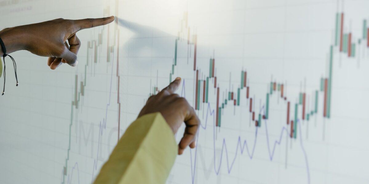 Hands pointing at a financial stock chart on a digital screen, highlighting data analysis and trends.