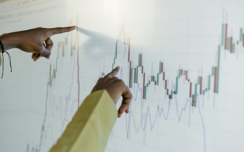 Hands pointing at a financial stock chart on a digital screen, highlighting data analysis and trends.