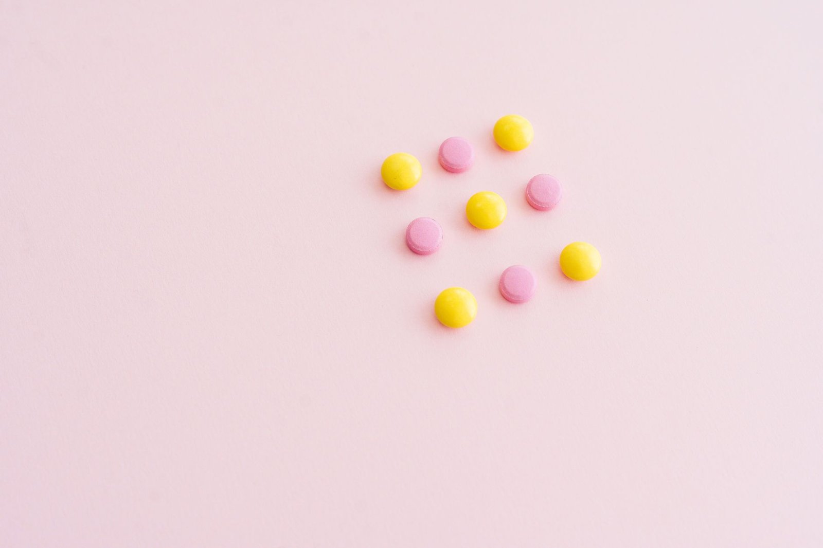 Vibrant yellow and pink pills arranged on a pink surface, offering ample copy space. Perfect for health themes.