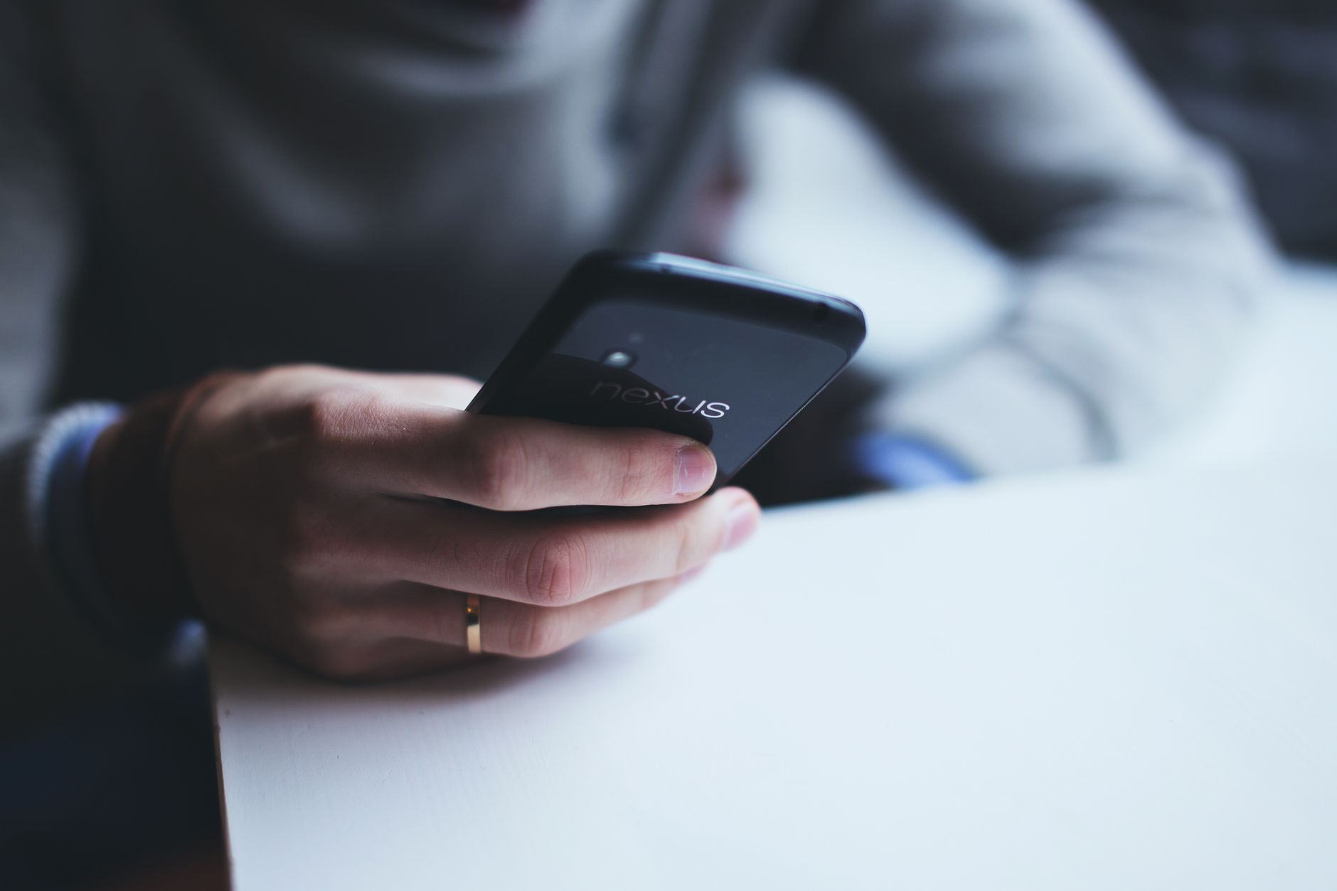 Close-up of a person holding a smartphone while sitting at a white table.