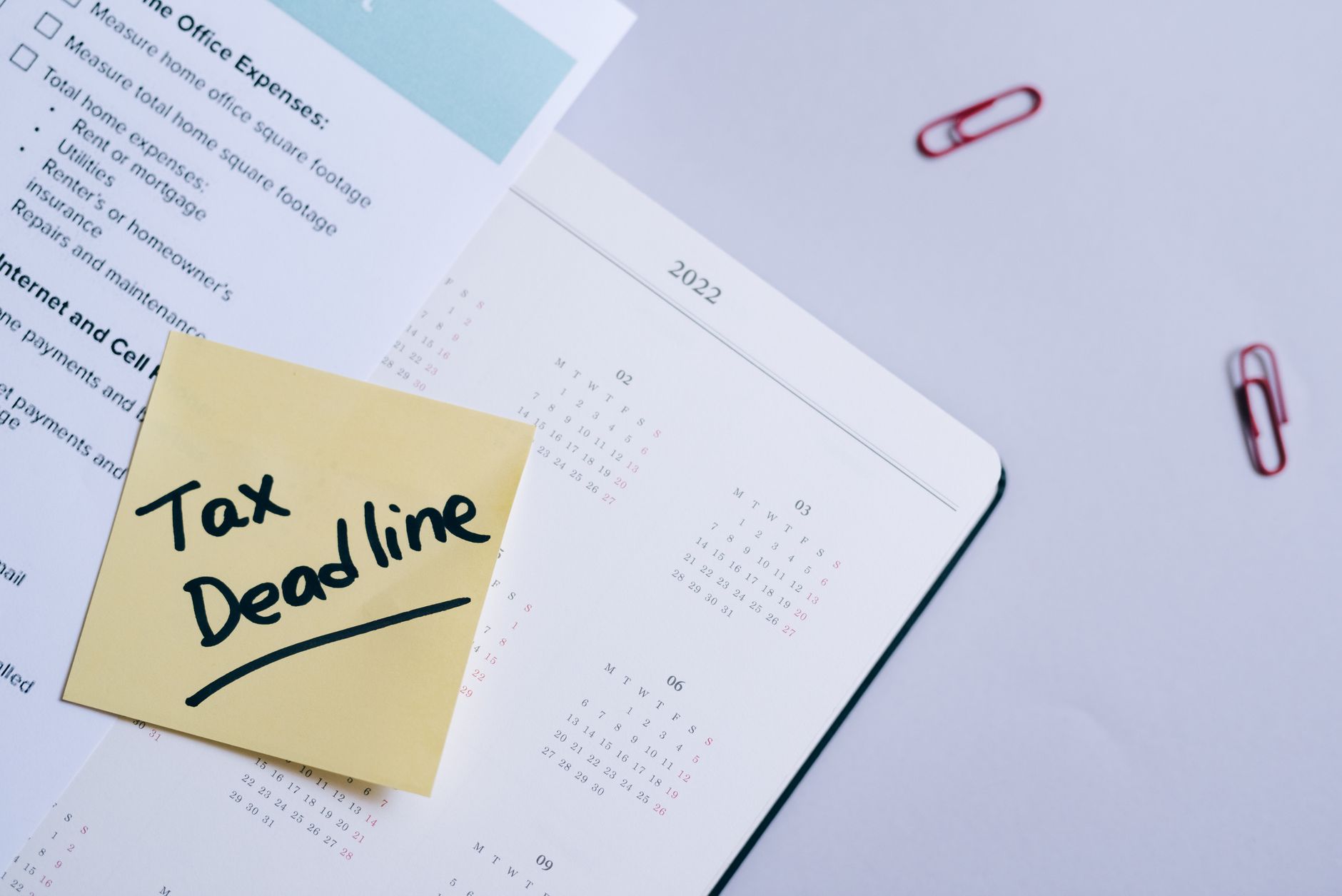 A sticky note highlights tax deadline on a calendar alongside documents, emphasizing financial planning.