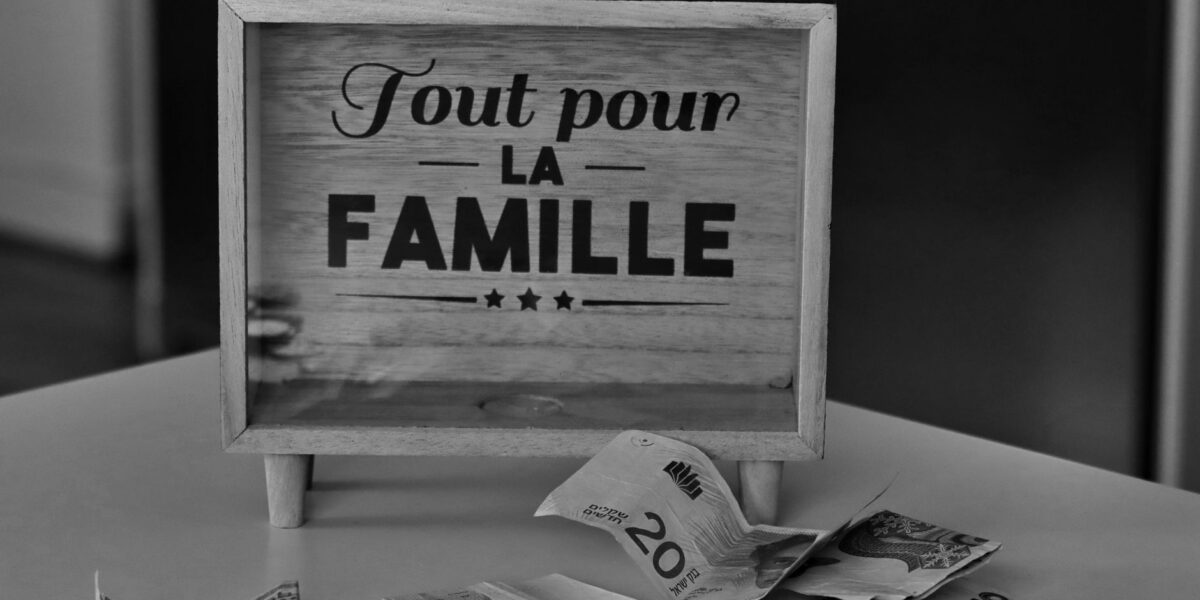 Black and white photo of a money box and various currencies on a table, symbolizing savings for family.