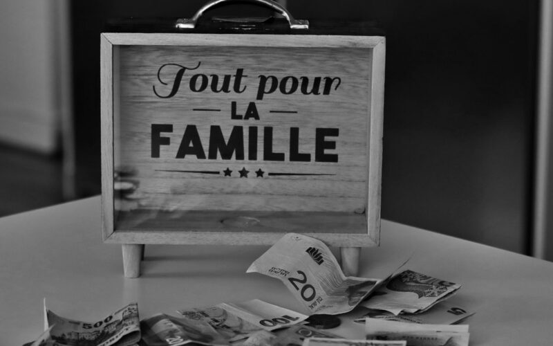 Black and white photo of a money box and various currencies on a table, symbolizing savings for family.