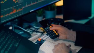 Business analysis with calculator and computer monitor displaying financial graphs and charts.