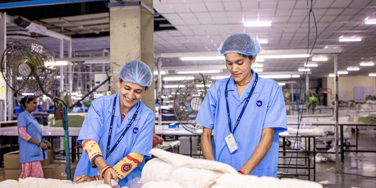 Smiling Indian factory workers in a textile factory wearing blue uniforms and hairnets, working diligently.