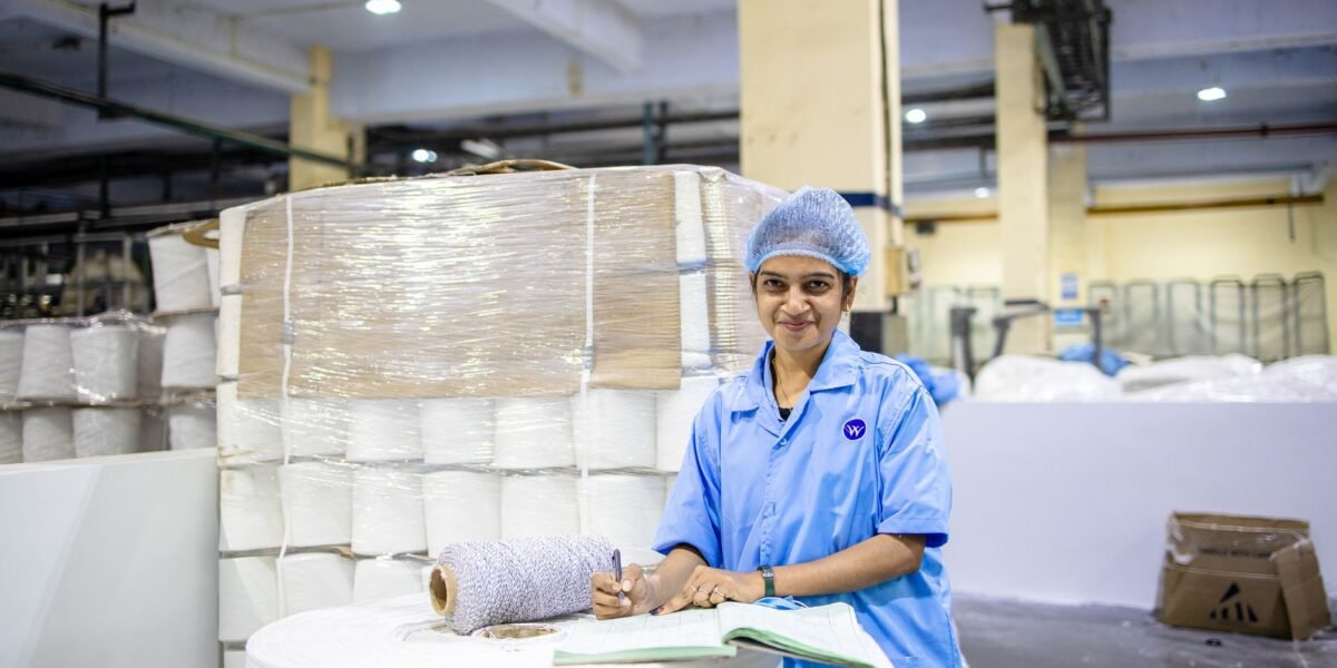 Smiling female textile worker taking notes in a factory with yarn stacks.