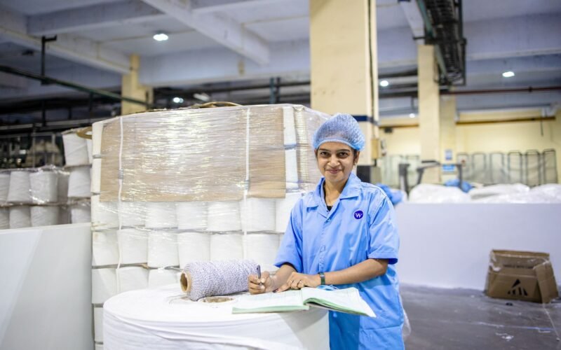 Smiling female textile worker taking notes in a factory with yarn stacks.