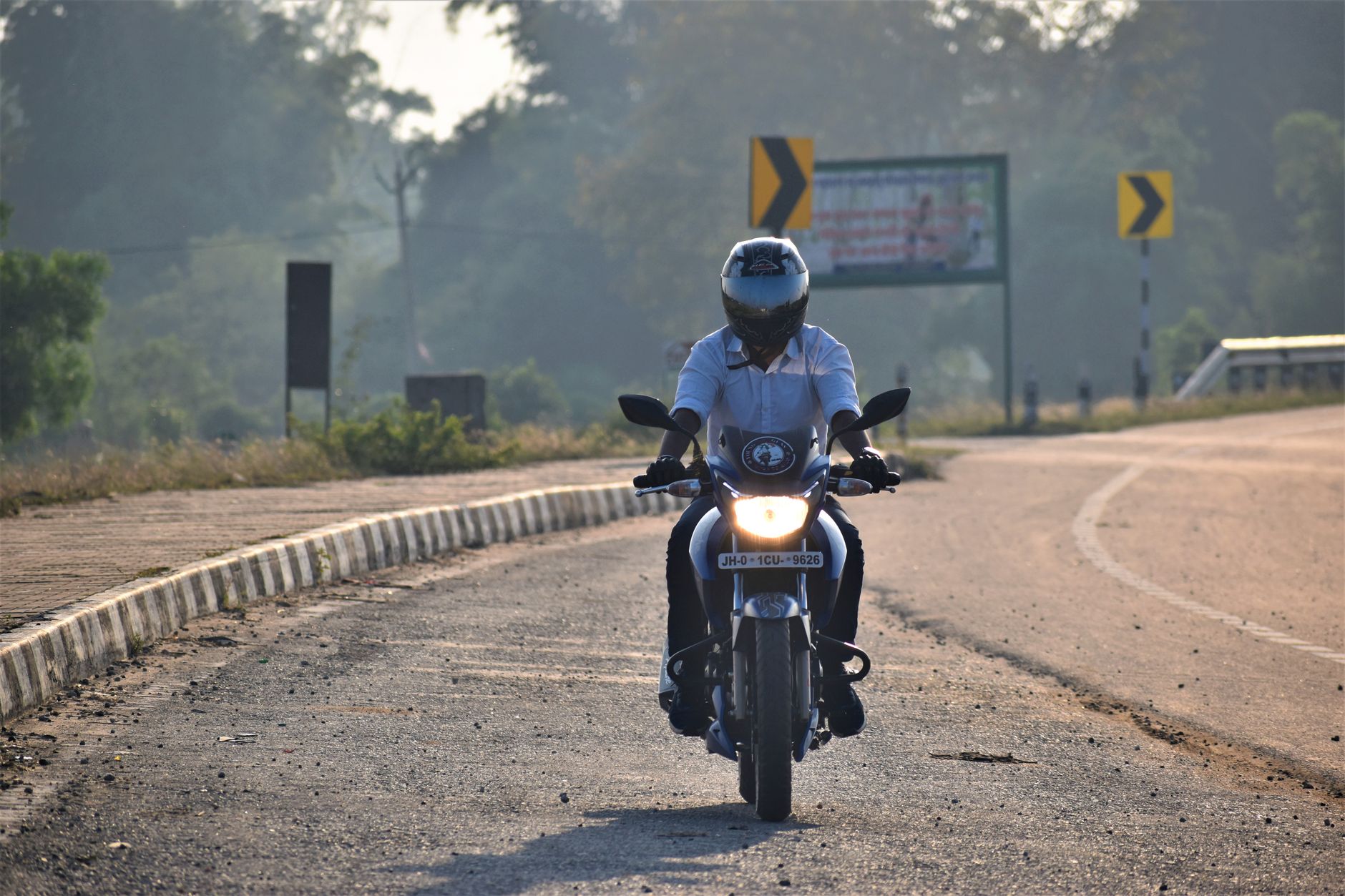 A motorcyclist wearing a helmet rides down a rural road in Ranchi, India. Captured in daylight.