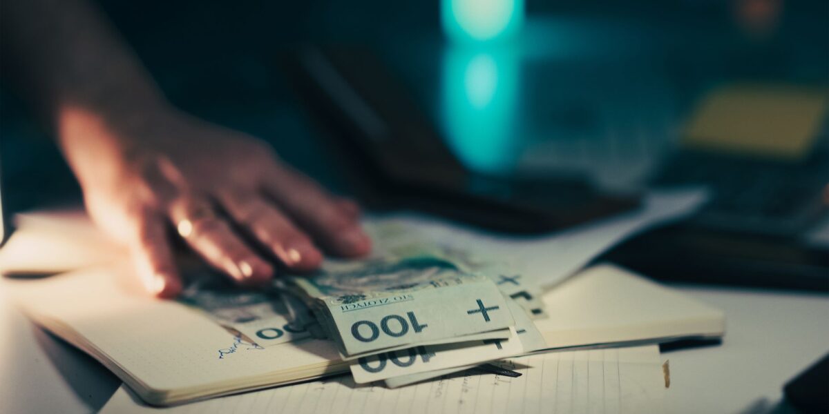 Close-up of hand reaching for banknotes on an office desk with a notebook and calculator.