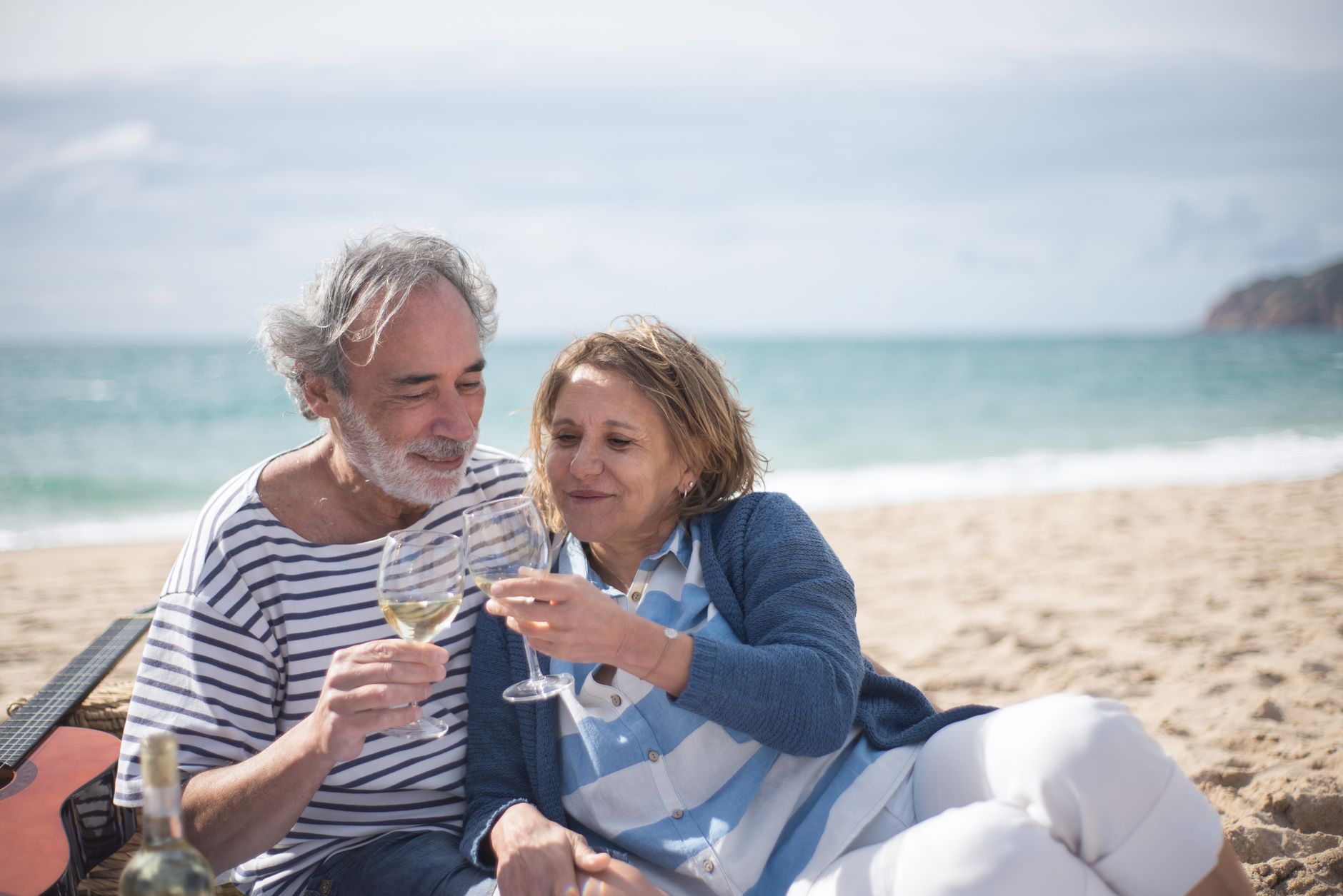 Happy senior couple enjoying a romantic moment with wine on a scenic beach in Portugal.