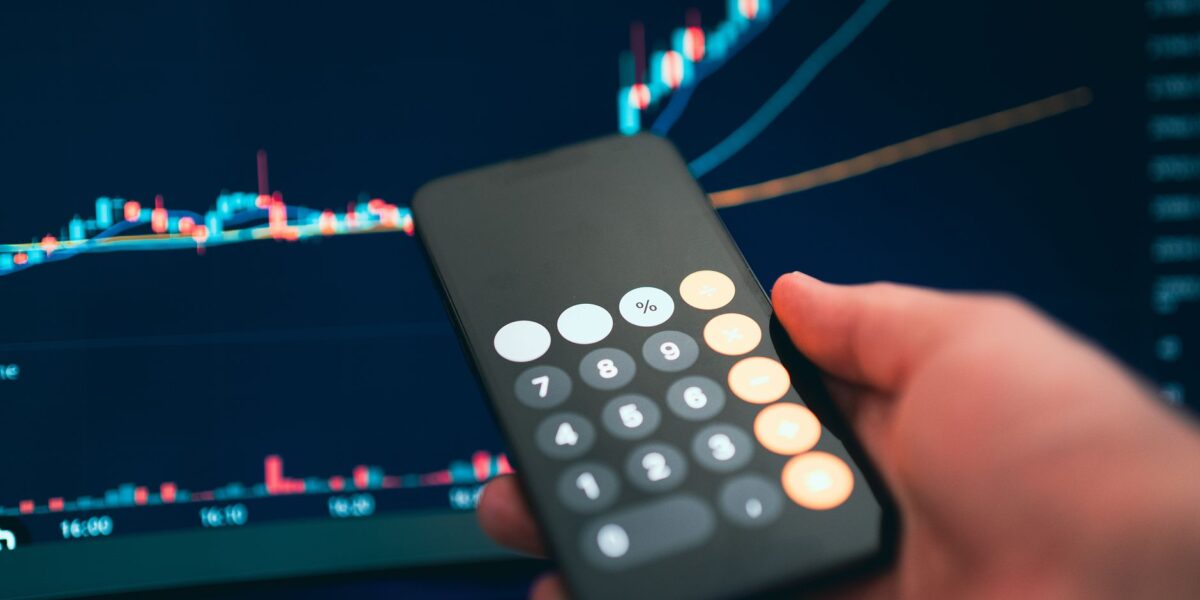 Close-up of a smartphone displaying a calculator with a financial chart in the background.