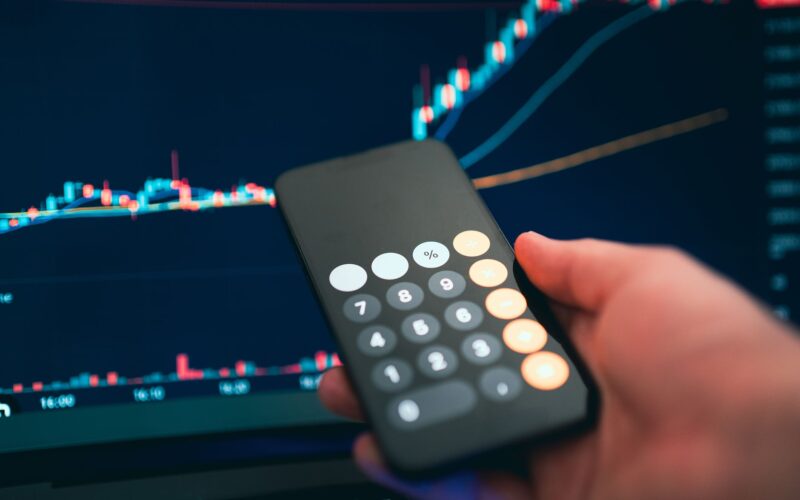 Close-up of a smartphone displaying a calculator with a financial chart in the background.