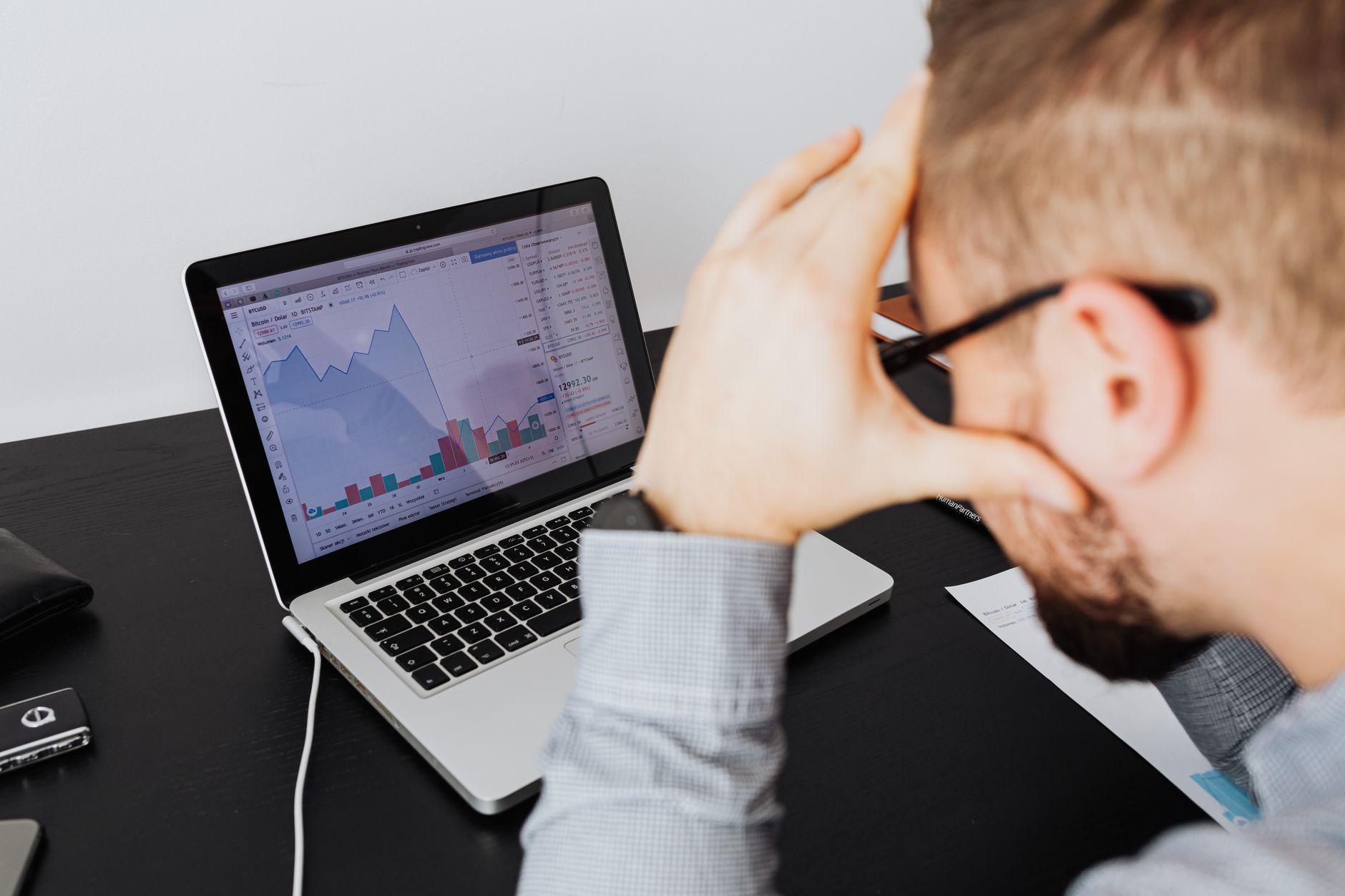 Over the shoulder view of a man analyzing financial data on a laptop screen.