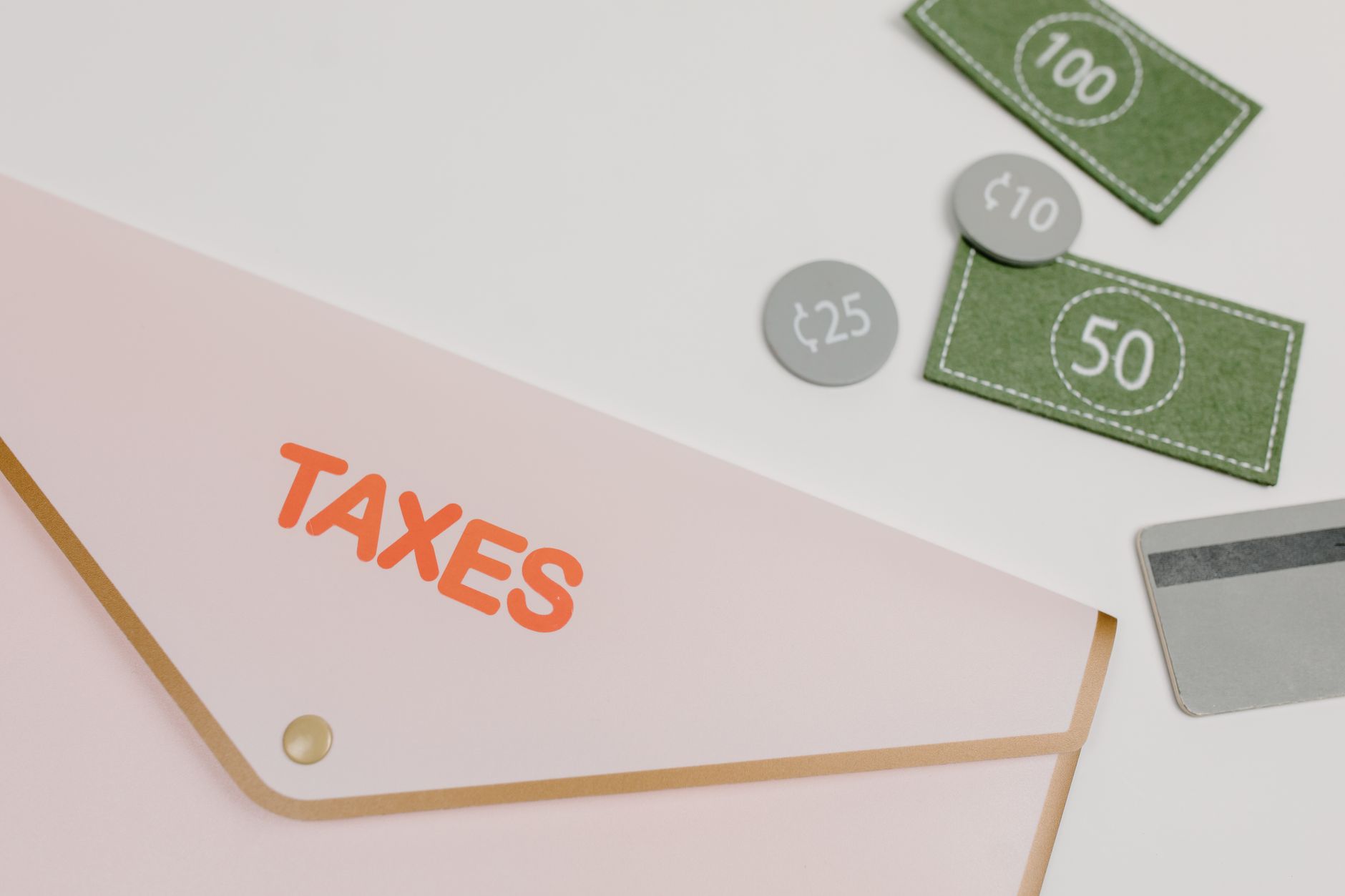 Pink envelope labeled 'TAXES' with play money and card on white background.