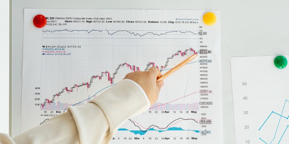 Close-up of a woman's hand pointing to data trends on a stock market chart using a pencil.