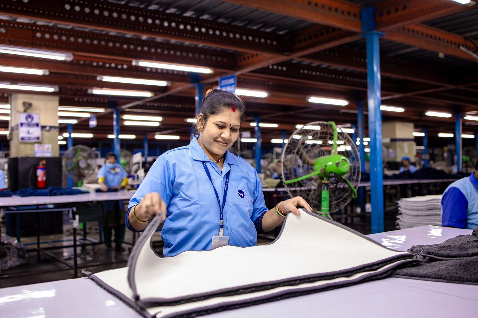 A woman in a blue uniform folding textiles in a brightly lit factory.