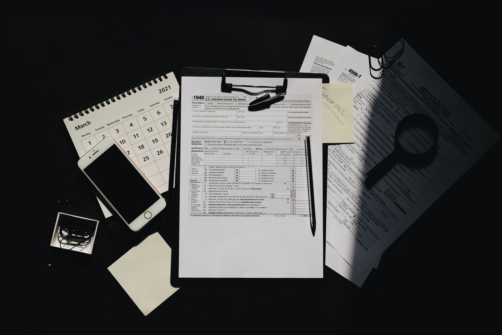 Flat lay of tax documents, calendar, and smartphone on a dark surface, symbolizing tax preparation.