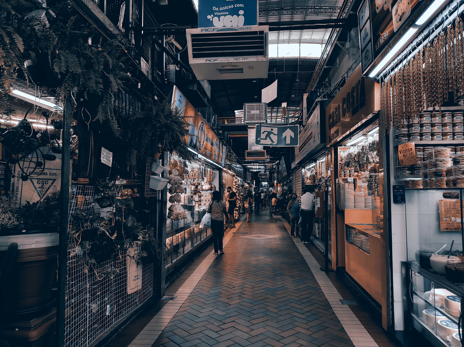 A vibrant indoor market scene with various stalls and shoppers exploring the goods on a busy pathway.