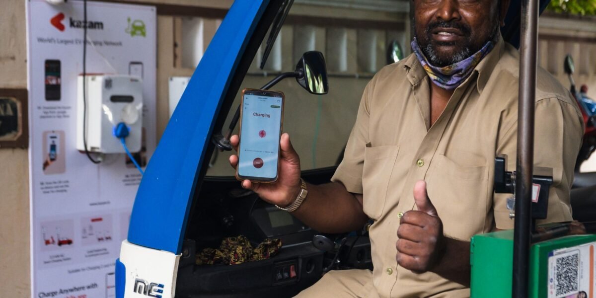 South Asian man using electric vehicle charging station in India, holding smartphone with app.