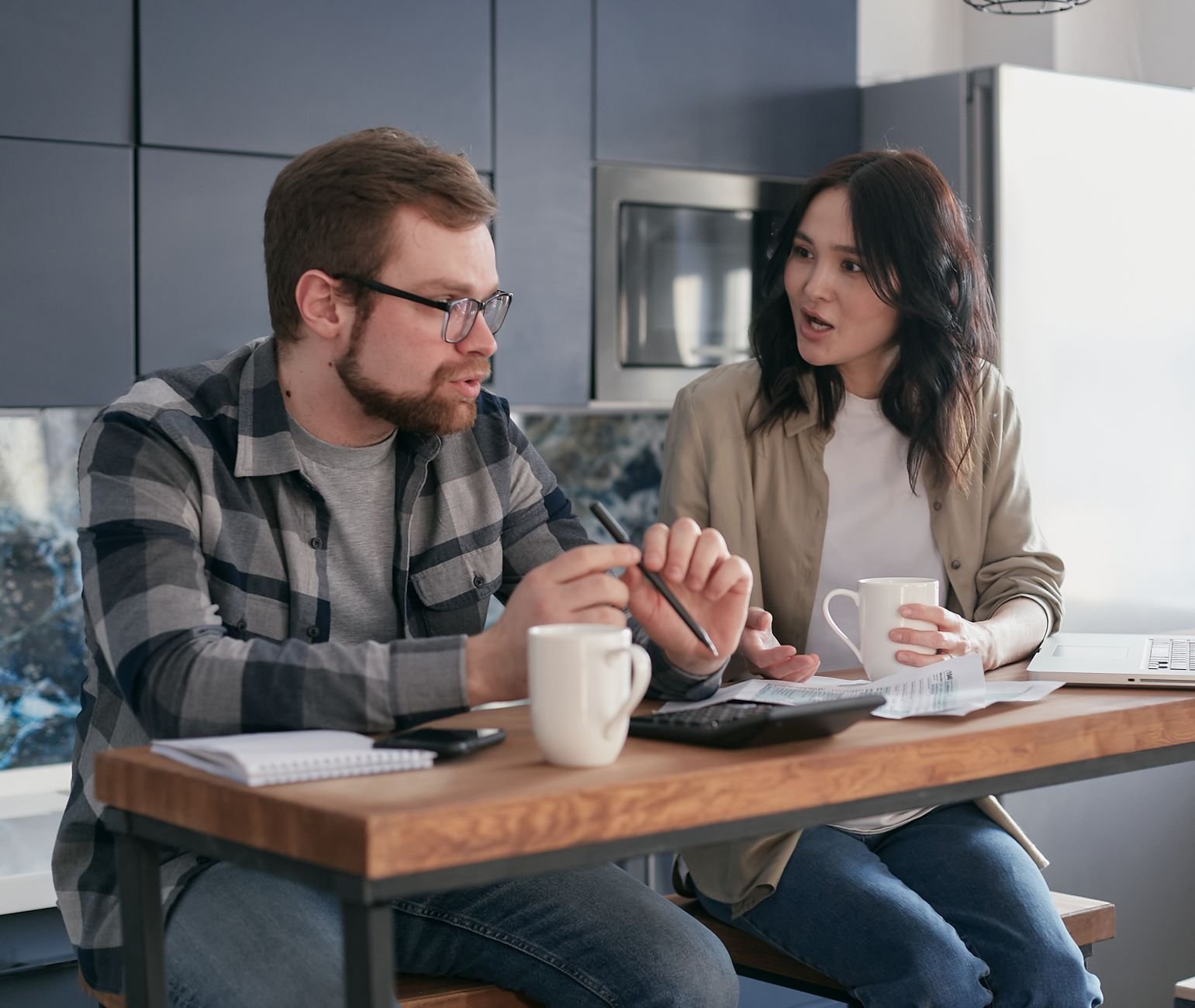 A couple managing finances with gadgets, documents, and coffee mugs at home.
