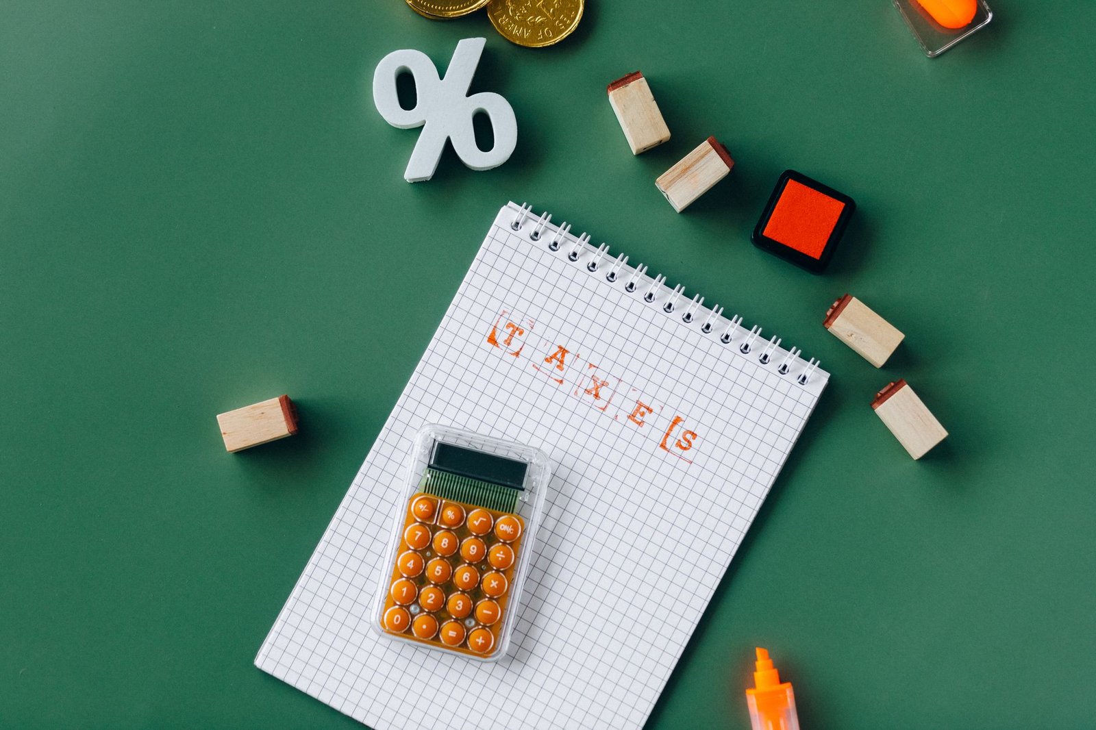 Flat lay of tax essentials with calculator, notebook, and stamps on a green background.