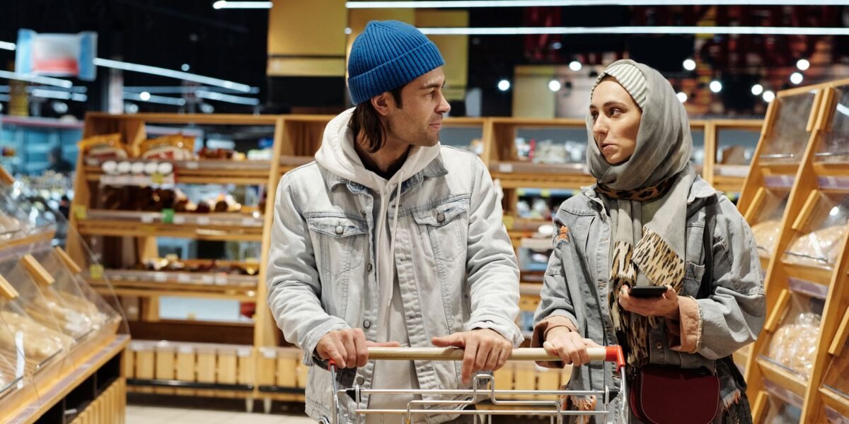 A diverse couple shopping for groceries in a supermarket aisle with a cart full of fruits.