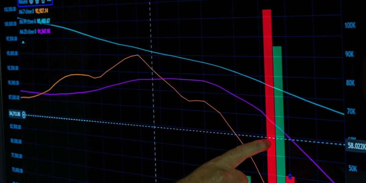 Hand pointing at a financial graph displaying cryptocurrency data analysis and trends.