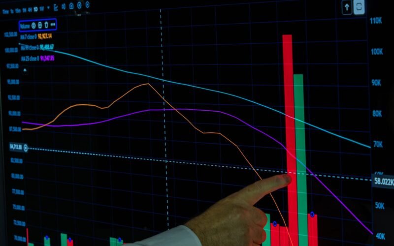 Hand pointing at a financial graph displaying cryptocurrency data analysis and trends.