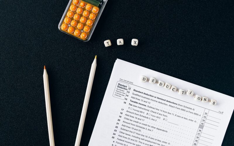 Flat lay of tax form, pencils, and calculator on black background, emphasizing tax deductions.