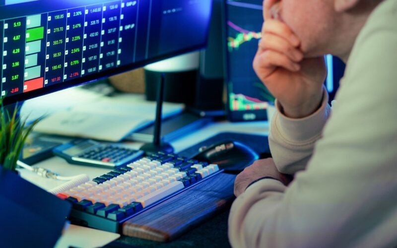 A stock trader intensely analyzing financial market data displayed on multiple screens in a modern office.
