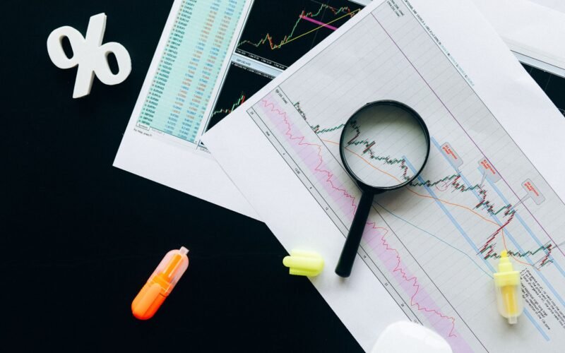 High-angle view of financial charts, showcasing stock market analysis with magnifying glass and highlighters.