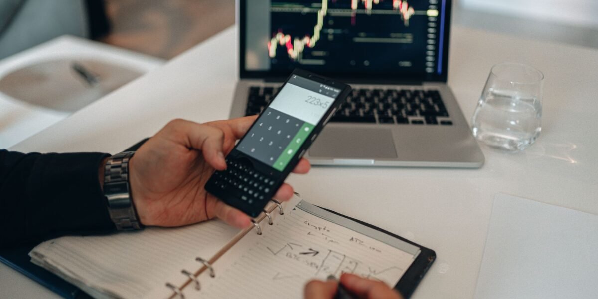Close-up of a person using a calculator and laptop with stock charts for financial analysis.