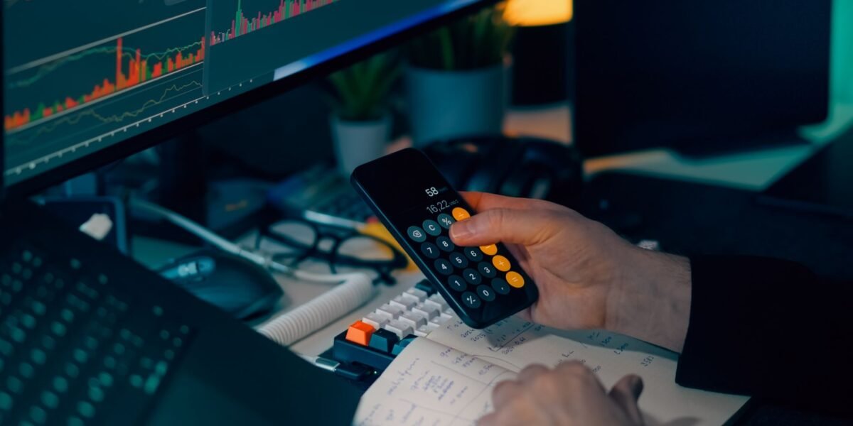 Business analysis with calculator and computer monitor displaying financial graphs and charts.